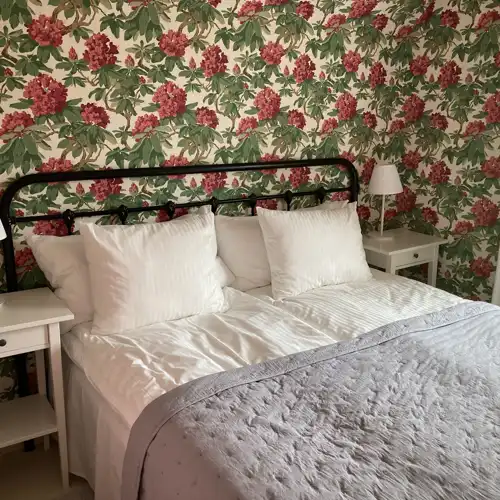 dubbelsäng med vita bordslampor på sidorna mot en rosa blommig tapet