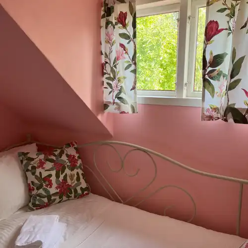 fönster med blommig gardin och en enkelsäng under, rosa väggar