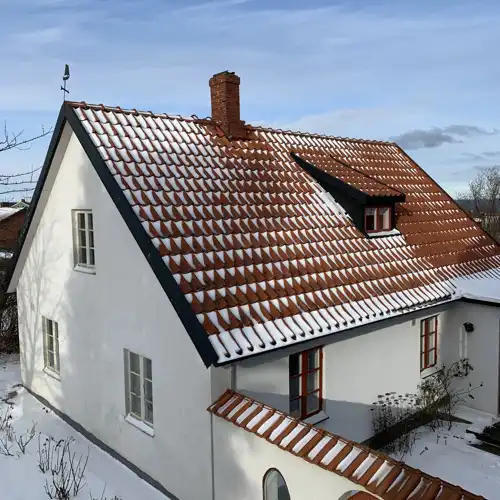 vitt hus snett uppifrån med lite pudrig snö på taket och i trädgården