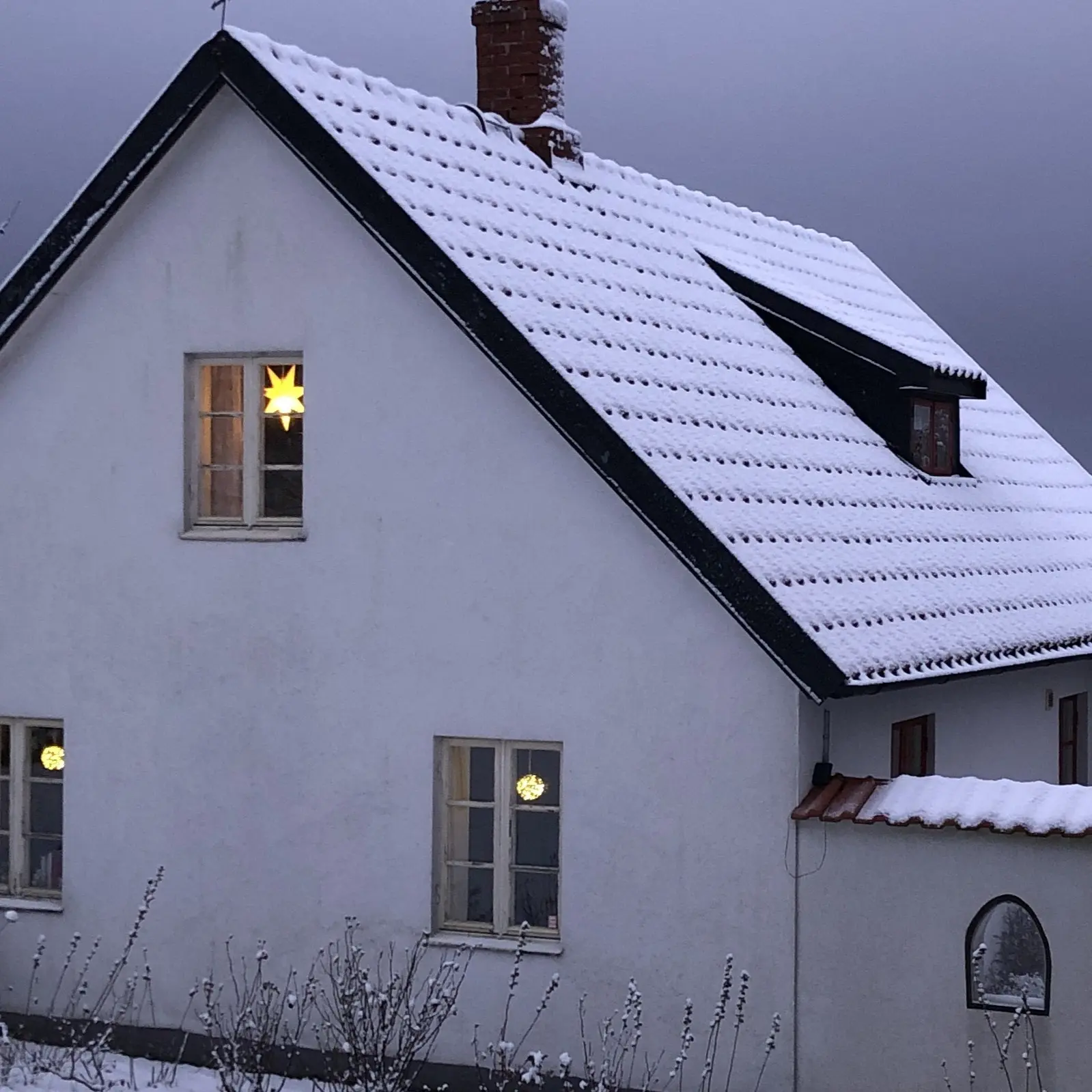 gavel av vitt hus på kvällen med adventsljus i fönstren