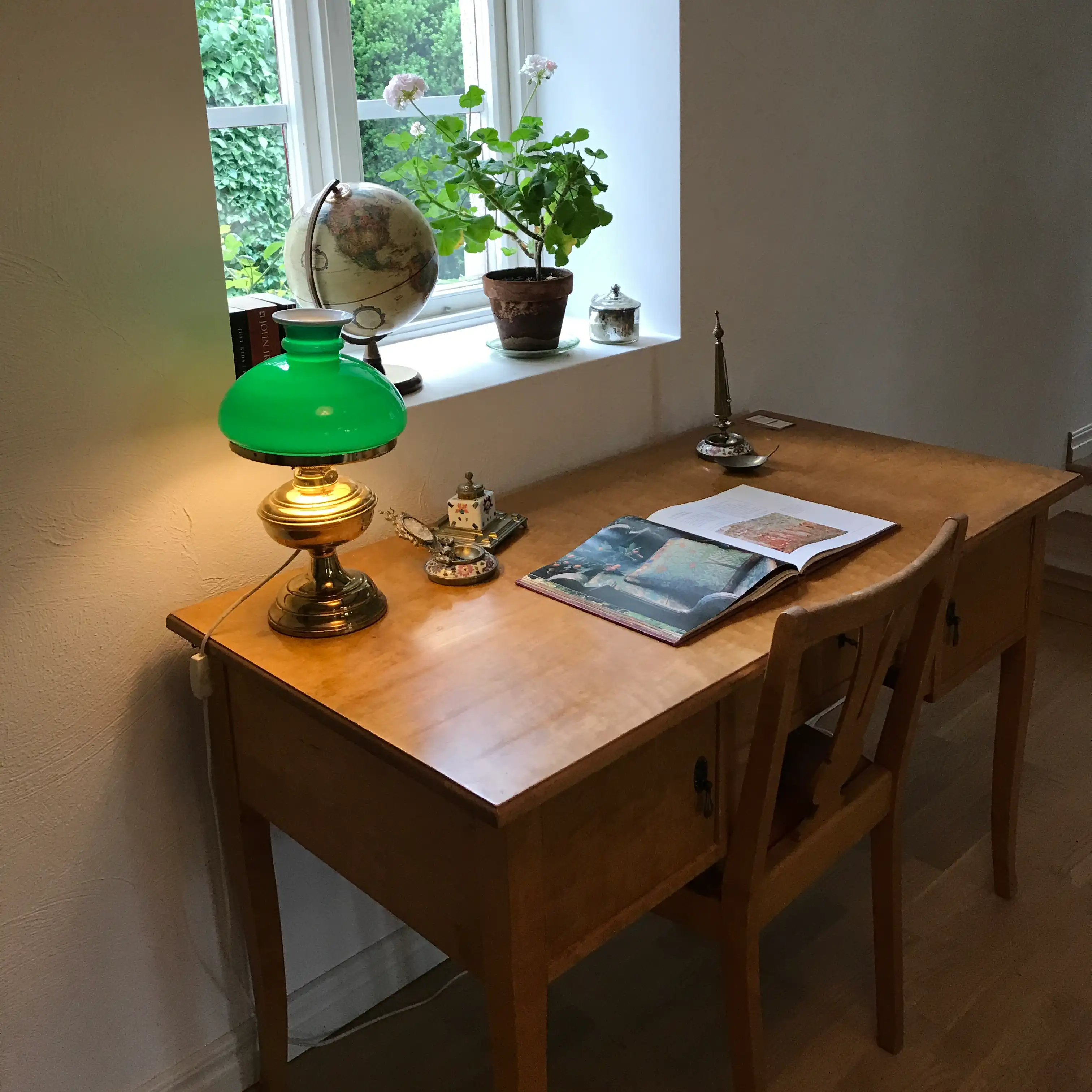 skrivbord med grön lampa och en öppen bok