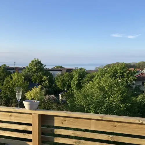 balkongräcke i trä med utsikt över träd och havet i bakgrunden